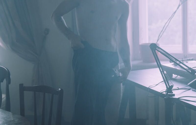 Topless Man in Black Pants Standing Near Black Wooden Table